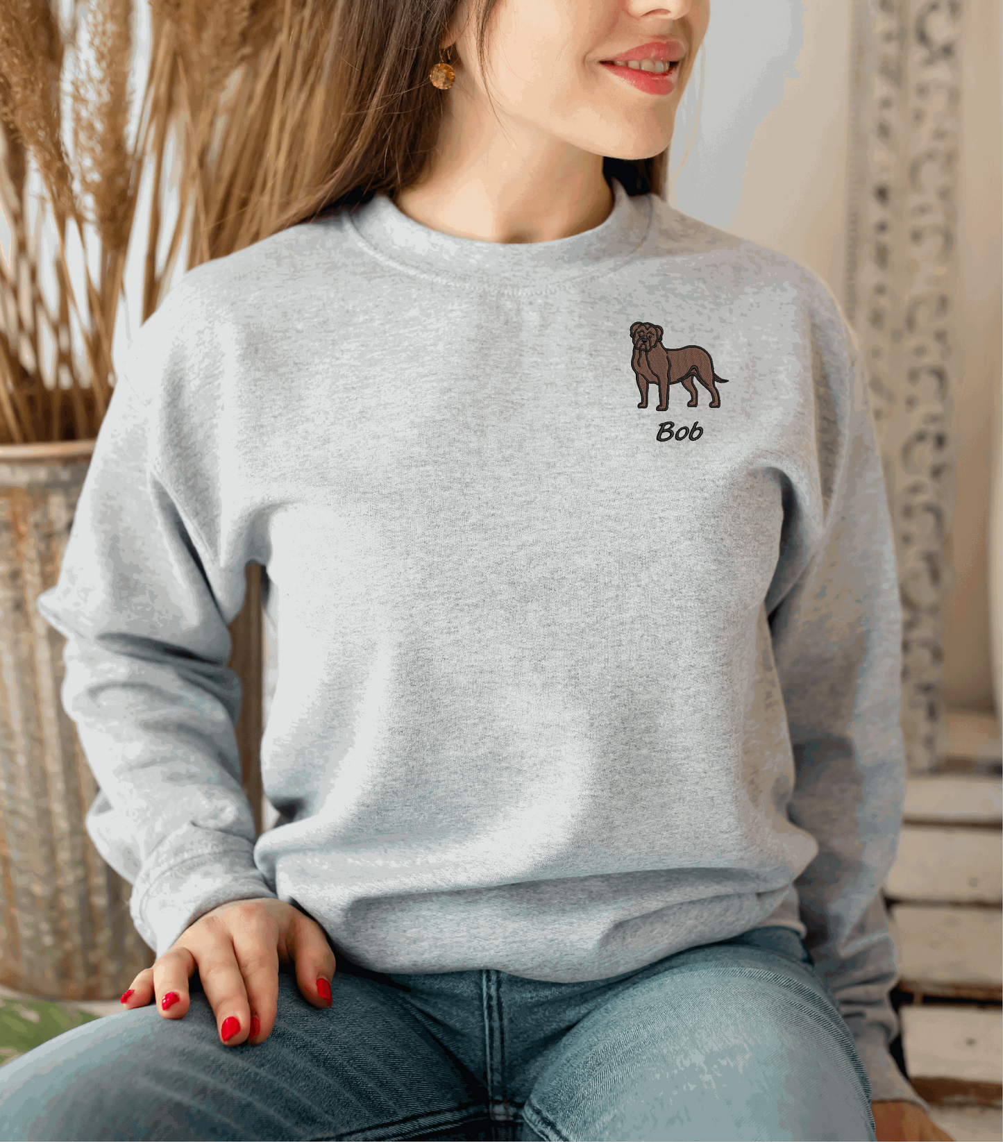 a woman sitting on a chair wearing a grey sweater with a dog embroidered on the