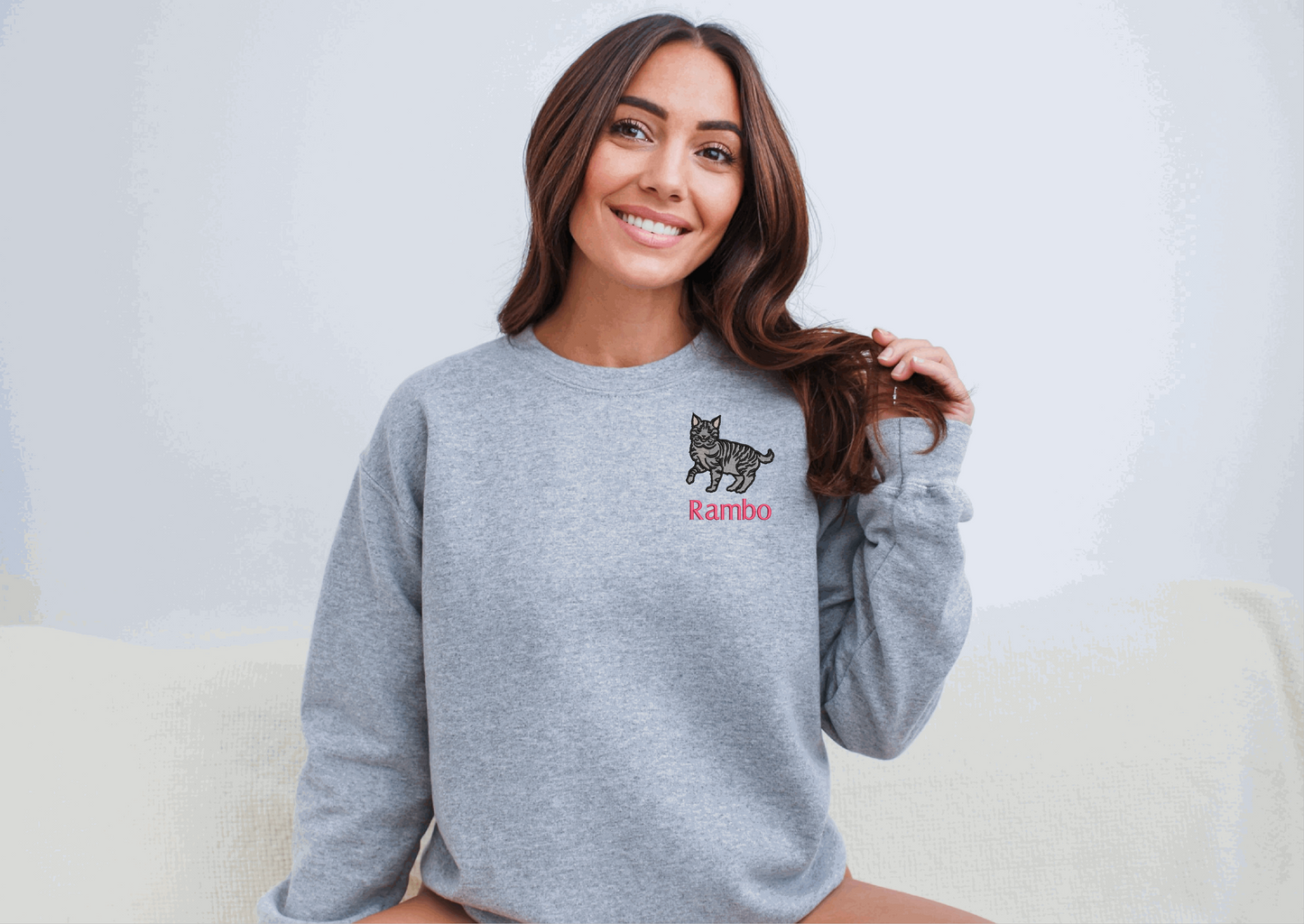 a woman sitting on a couch wearing a grey sweater with a cat on it